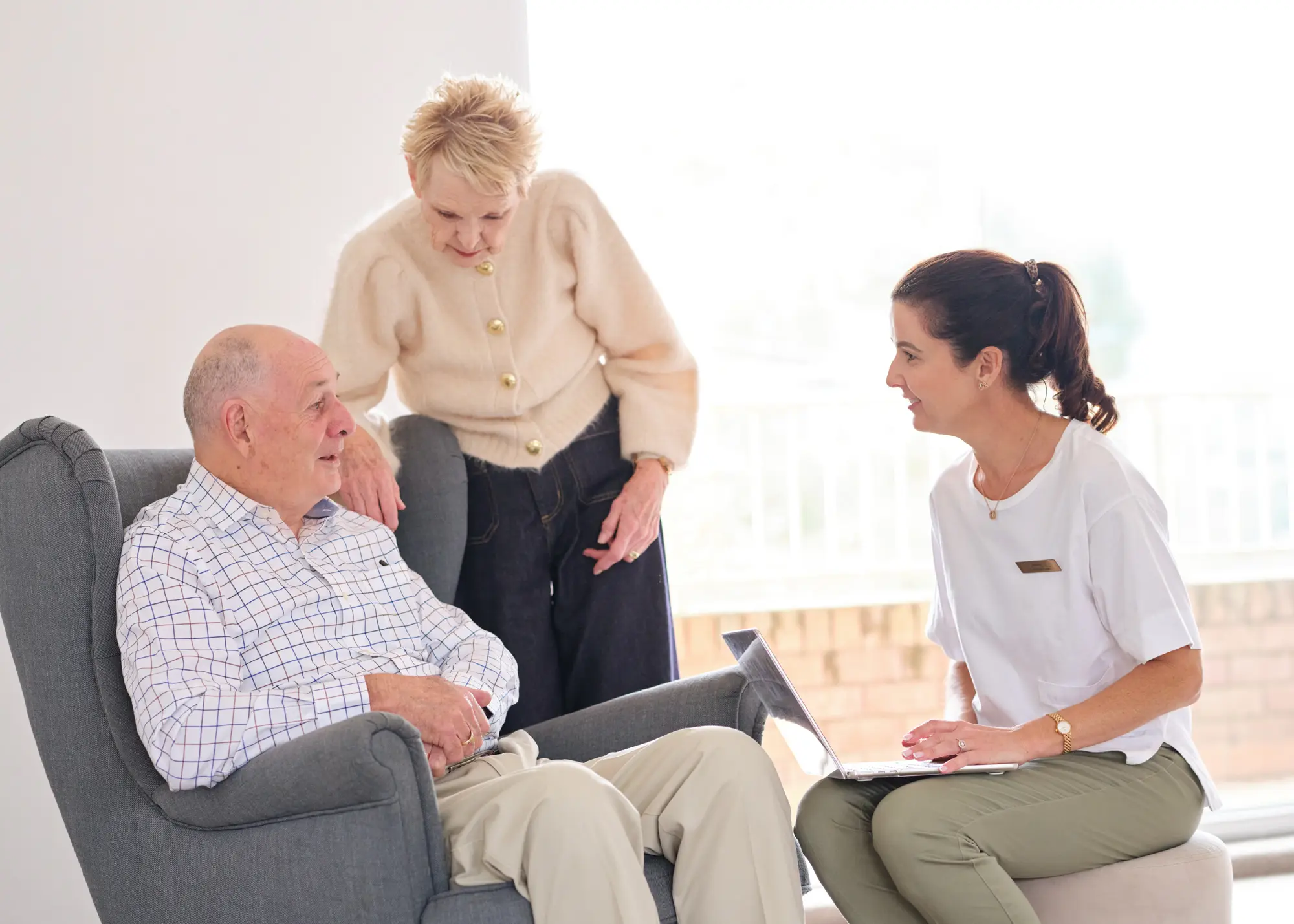 A care adviser showing a home care plan on a laptop to an older couple in their lounge room.